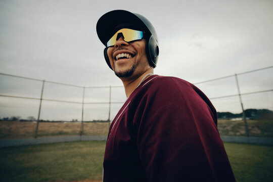 Smiling baseball player wearing polarized sunglasses on field, exuding a professional and confident demeanor