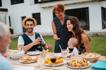 Family sitting at table and eating delicious food during spring family barbecue.