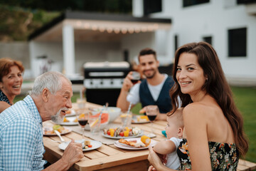 Family sitting at table and eating delicious food during spring family barbecue.
