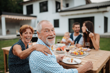 Family sitting at table and eating delicious food during spring family barbecue.