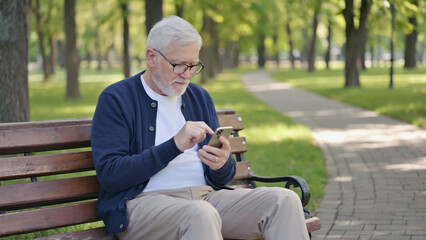 Fototapeta premium A person relaxing on a park bench, focused on their mobile device