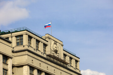 Russian flag on the Parliament building in Moscow against blue sky with clouds. Facade of State...