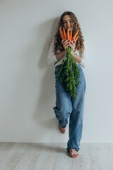 Portrait of smiling beautiful girl showing carrot on white background
