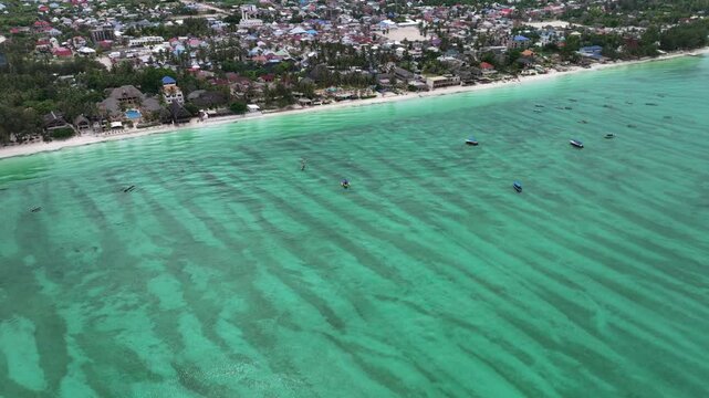 descending and flying toward the beach with turquoise water, near central part of Paje Downtown, located on island of Unguja, part of Zanzibar in Tanzania - 4k aerial video footage