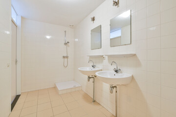 A simple and modern bathroom featuring twin sinks, elegant mirrors, and tiled walls. The design emphasizes cleanliness and functionality.