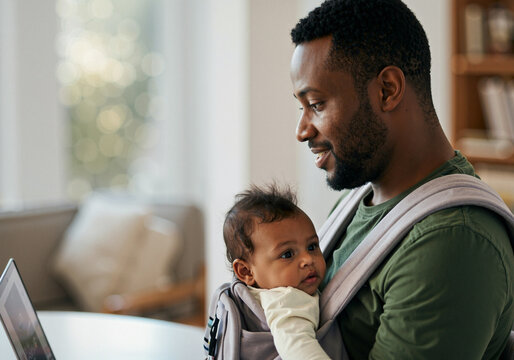 Young father working from home while holding his baby close to him in a carrier