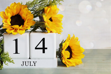 Bastille Day. White wood calendar blocks with the date July 14th and beautiful sunflower bouquet with bokeh. Selective focus with blurred background. 