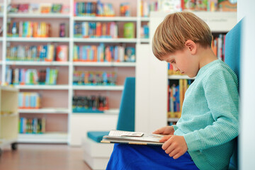 Young boy is sitting in library setting reading book. Child is completely engrossed in reading...