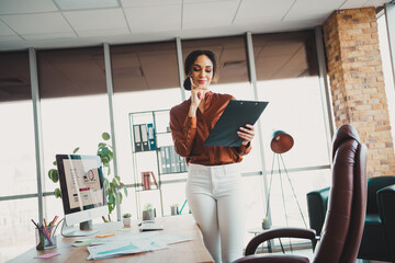 Young businesswoman evaluating documents on clipboard in modern office workspace with elegant interior design and natural light.