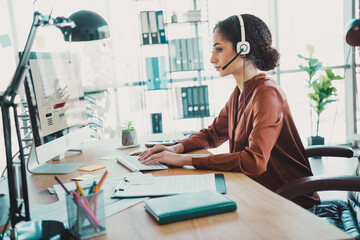 Young businesswoman at her desk wearing a headset while focused on work, in a modern office space...
