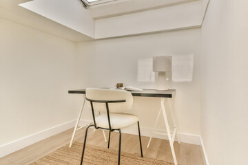 A clean, modern workspace featuring a simple desk, chair, and lamp, enhanced by soft natural light from the skylight above.