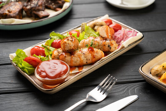 German cuisine. Crispy fried grilled chicken sausages with tomato slices, lettuce leaves, and ketchup on dark wood background. Tasty and hearty meal in rustic style.