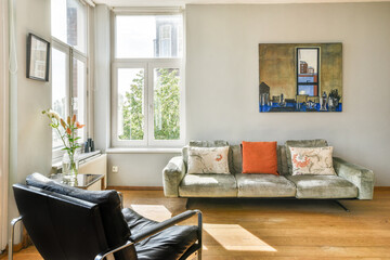 A stylish modern living room featuring a comfortable sofa, artistic decor, and bright natural light filtering through large windows.
