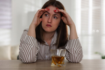 Alcohol addiction. Woman at wooden table with glass of whiskey indoors, selective focus