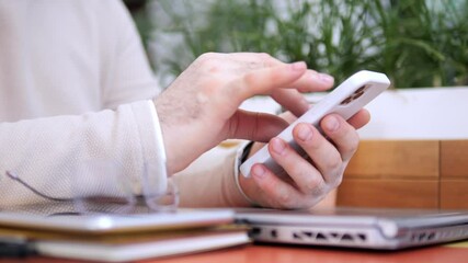 Person is using a cell phone while sitting at a desk with a laptop and a book. Concept of productivity and focus, as the person is engaged in work or study. The presence of the laptop