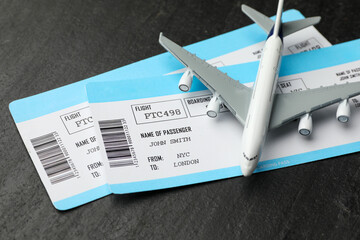 Travel agency. Flight tickets and plane model on dark textured table, closeup