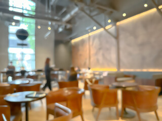 Blurred interior of a modern cafe with wooden chairs and tables, warm lighting, and large windows, creating a cozy and inviting atmosphere for social gatherings and relaxation.