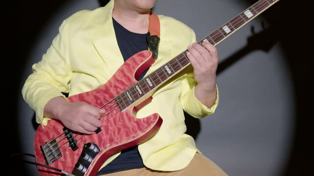 エレキベースを座ってピック奏法で演奏している男性
