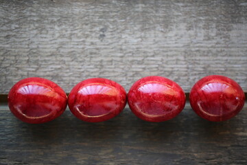 Four  Easter red eggs are lying on the wooden table. The light is beautifully reflected in the eggs through the balcony railing.