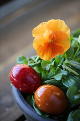 Easter eggs are lying next to an orange pansy flower. The background is a wooden table.
