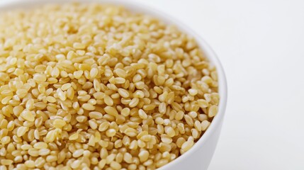 Golden bulgur wheat in white ceramic bowl on bright background
