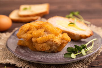 Chicken Schnitzel on gray plate with microgreen on brown wooden background and linen textile. side view, selective focus