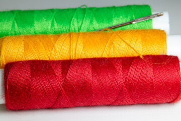 Colorful sewing threads in red, yellow, and green with a metal needle.