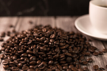 A pile of coffee beans on a wooden table. Coffee beans and a cup of coffee