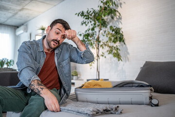 Stressed man packing clothes into suitcase at home before trip
