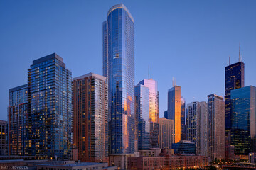 Naklejka premium Cityscape at dusk, showcasing various modern skyscrapers reflecting warm sunset light, creating a vibrant urban scene