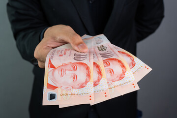 Business in black suit hands over dozens of singapore dollars banknotes, with grey background