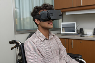 A south asian boy sits in a wheelchair wearing virtual reality goggles, focused and engaged, in a modern office setting with a laptop in the background