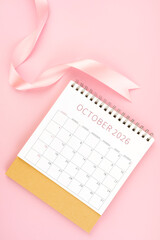 October 2026 desk calendar with pink ribbon, Flat lay.