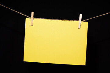 Cartulina amarilla colgada con pinzas sobre fondo negro