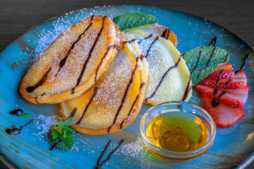 sweet pancakes with syrup, powdered sugar, honey and strawberries served on a blue plate