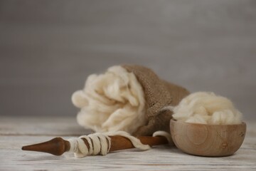 Soft white wool and spindle on wooden table. Space for text