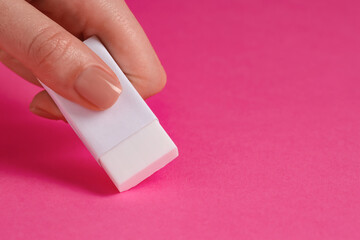 Woman using eraser on pink background, closeup. Space for text