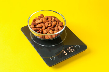 Electronic kitchen scale with bowl of almond nuts on yellow background, closeup