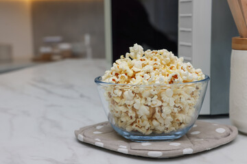 Tasty popcorn in bowl near microwave oven on white marble table indoors, space for text
