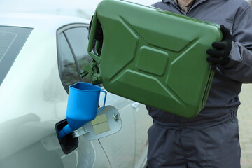 Man pouring fuel from canister into funnel outdoors, closeup