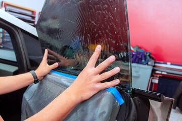 Technician applies window tint film on car door at an auto shop, ensuring proper adhesion coverage.