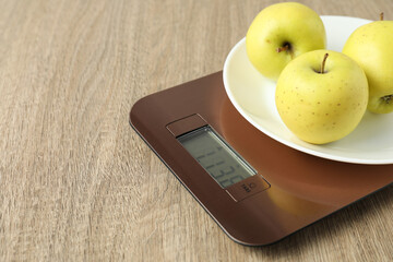 Modern electronic kitchen scale with apples on wooden table, closeup. Space for text