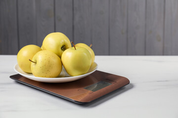 Modern electronic kitchen scale with apples on white marble table, closeup. Space for text