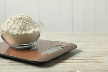 Modern electronic kitchen scale with bowl of flour on wooden table, closeup. Space for text