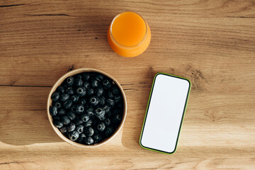 Glass of juice, blueberries and smartphone with blank screen on table, top view.