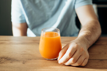 Glass of orange juice in male hand at home, close up.
