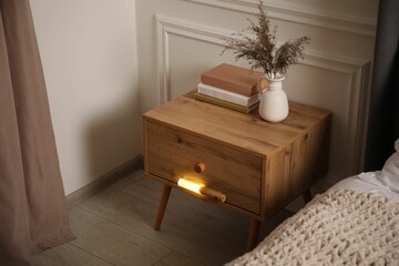 Glowing modern LED lamp on wooden bedside table indoors