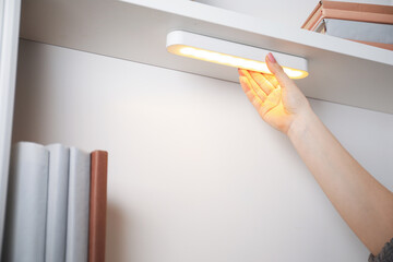Woman putting modern LED lamp onto shelf indoors, closeup