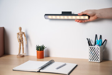 Woman putting modern LED lamp onto wall above desk, closeup