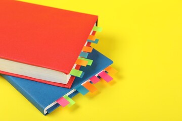 Books with colorful tabs on yellow background, closeup. Space for text